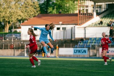 Stephanie Gerken springt zwischen zwischen zwei Spielerinnen Blau-Weiß Hohen Neuendorfs in die Luft und schaut dem Ball hinterher. Foto: Kai Heuser (@heuserkampf)