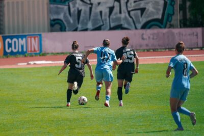 Vier Spielerinnen im Bild, mit dem Rücken zur Kamera. Vorne rechts verschwommen Henrike Sahlmannn mit blauem Trikot und der Rückennummer 8. Mittig im Bild, etwas weiter entfernt, deshalb kleiner: Leyila Aydin in hellblau mit der Rückennummer 47. Links und rechts von ihr jeweils eine Ingolstädterin, links Nummer 5, rechts Nummer 25. Foto: Kai Heuser (@heuserkampf).
