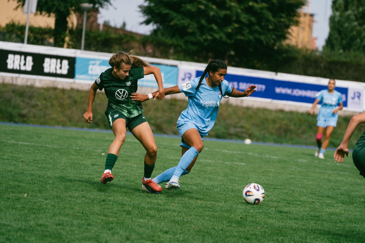 Die FC-Viktoria-Berlin-Spielerin Maya Hahn mit zwei langen geflochtenen dunklen Zöpfen und himmelblauem Trikot im Zweikampf mit einer Wolfsburgerin im dunkelgrün/hellgrünen Trikot.